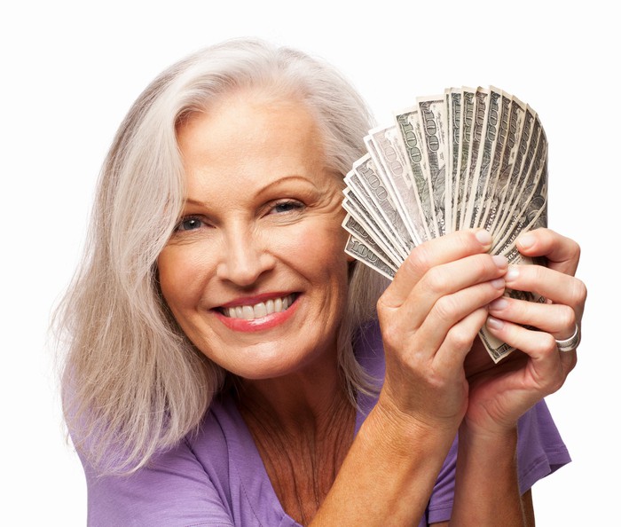 Smiling older woman holding fan of hundred dollar bills