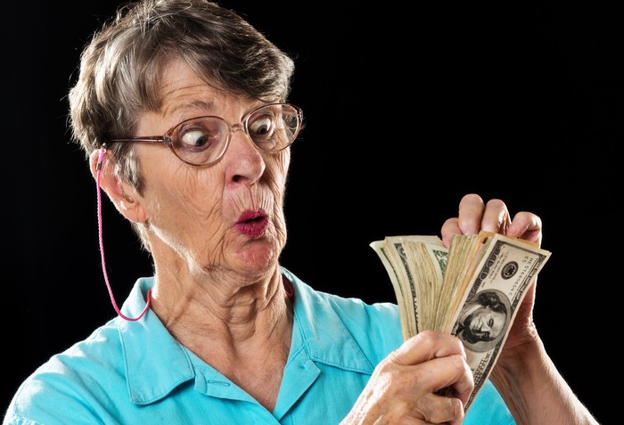 An older woman is looking surprised and amazed as she counts her cash.