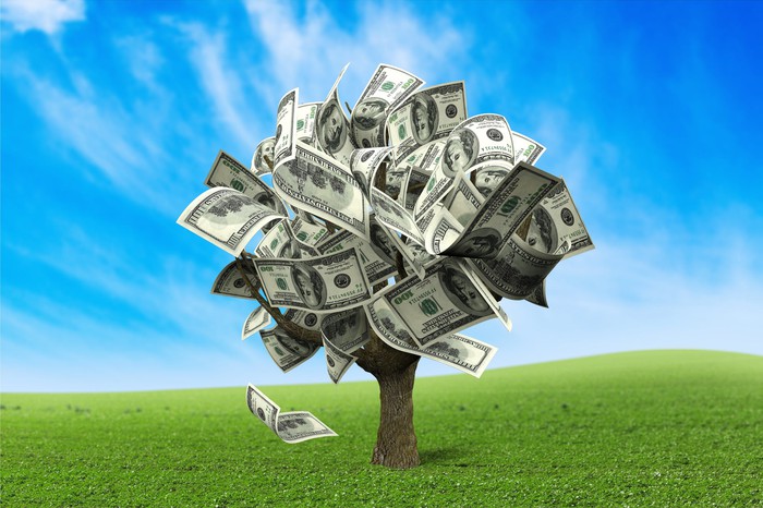 A tree made of money stands in a green field.