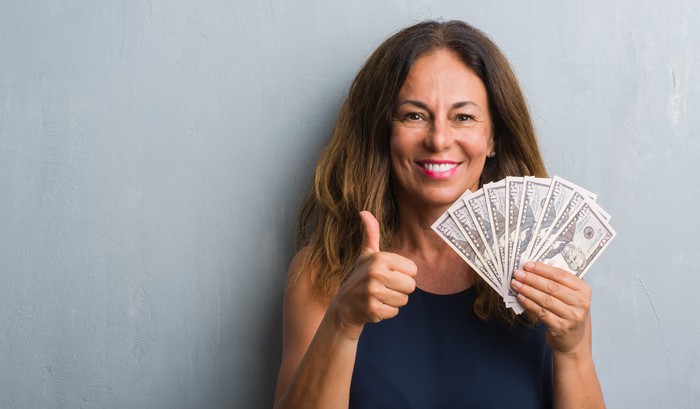 Woman holding cash and giving a thumbs-up 