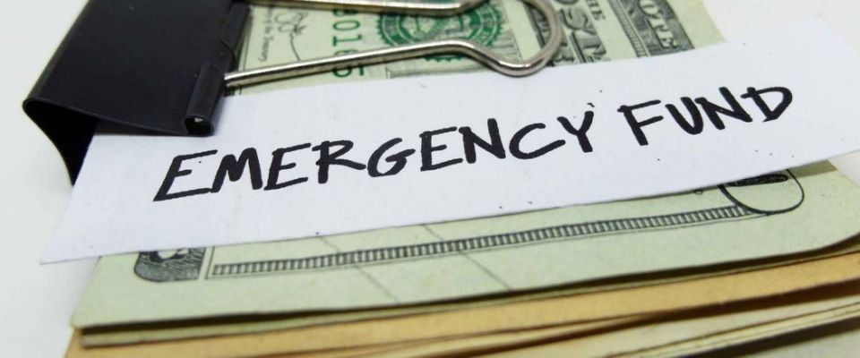 Closeup of US dollars in paper clip on white background with note written EMERGENCY FUND