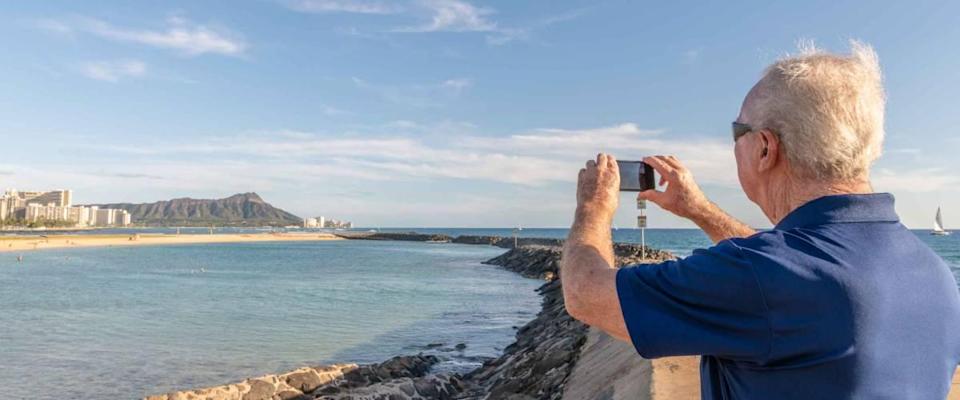 A senior man takes a photo of Diamond Head while on a family trip to Honolulu, Hawaii.