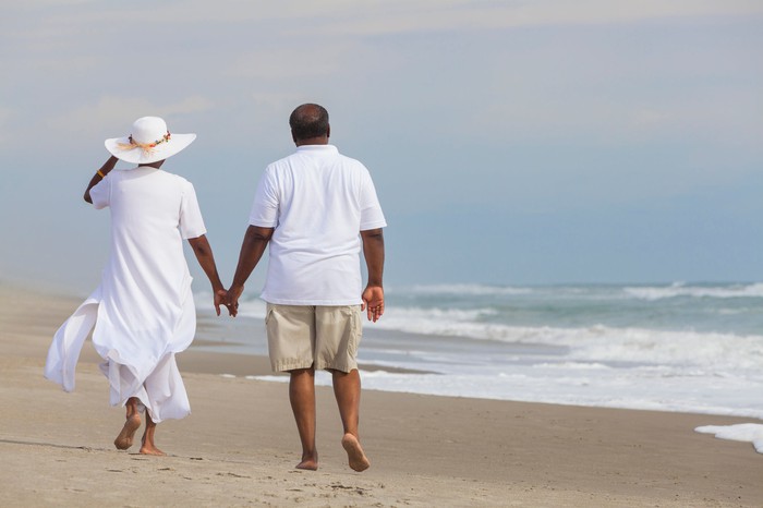 Couple holding hands walking down a beach.