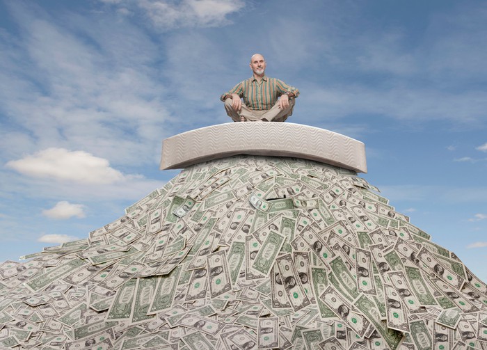 Senior man sitting atop a rising pile of money.