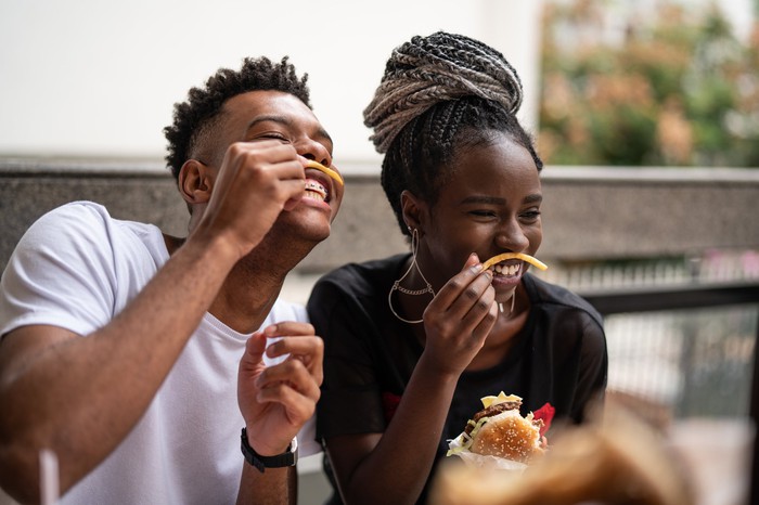 Two young people playing with their french fries in a fast-food restaurant.