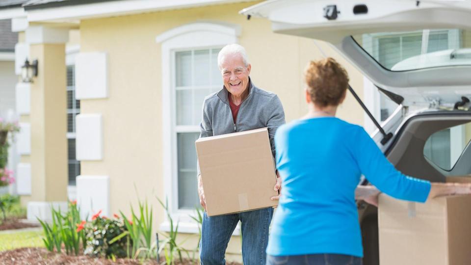 A senior couple lifting cardboard boxes into or out of the back of a car