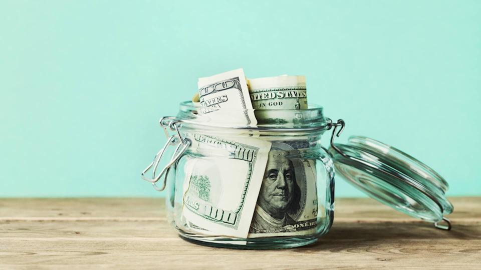 Dollar bills in glass jar on wooden table.