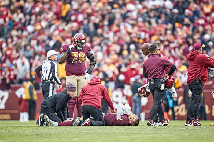 Alex Smith lies on the field with his hands over his face after breaking his right leg during a 2018 game