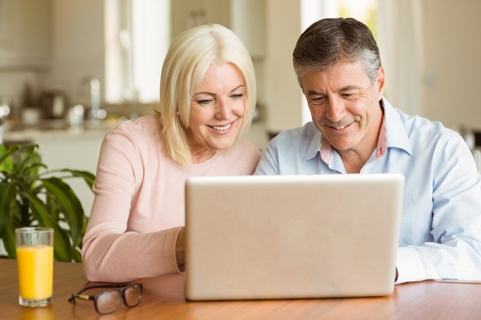 An older man and woman at a laptop, smiling.