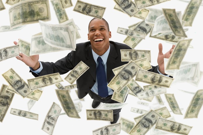 Smiling man with money falling all around him.