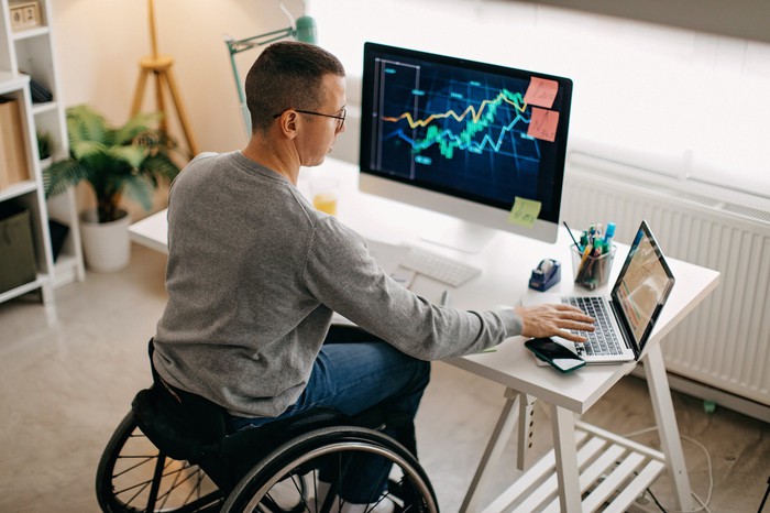 Person sitting in front of computer and laptop looking at investment information.