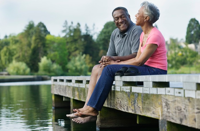 Two seniors sitting on pier over lake.